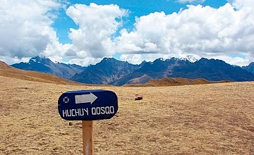 Letrero ‘Huchuy Qosqo’ en la ruta de trekking, Cusco, con vista amplia de montañas al fondo